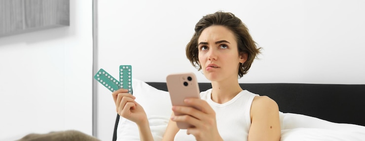 Foto gratuito retrato de una mujer pensante acostada en la cama con píldoras sosteniendo medicamentos y un teléfono móvil buscando