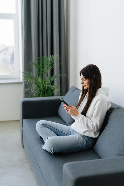 Retrato de mujer pensativa de ensueño sosteniendo un teléfono inteligente en las manos mirando hacia otro lado divirtiéndose placer armonía comodidad comodidad sofá