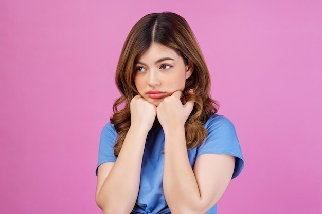 Foto gratuita retrato de una mujer pensativa, miserable y abatida, con una camiseta informal, manteniendo las manos bajo la barbilla, aislada sobre un fondo rosado