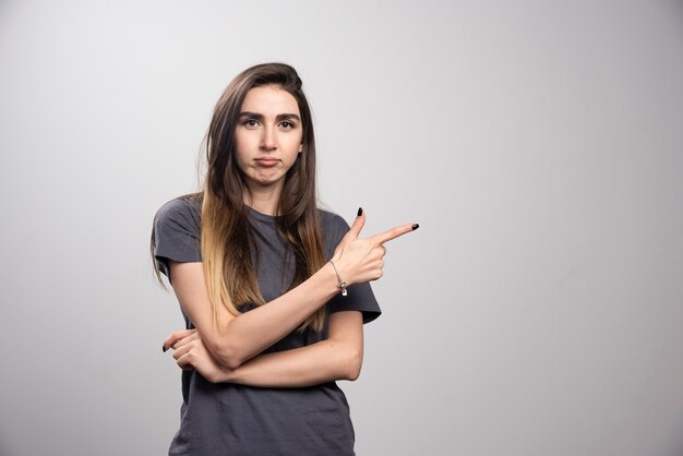 Retrato de mujer de pie y apuntando a algún lugar sobre un fondo gris.