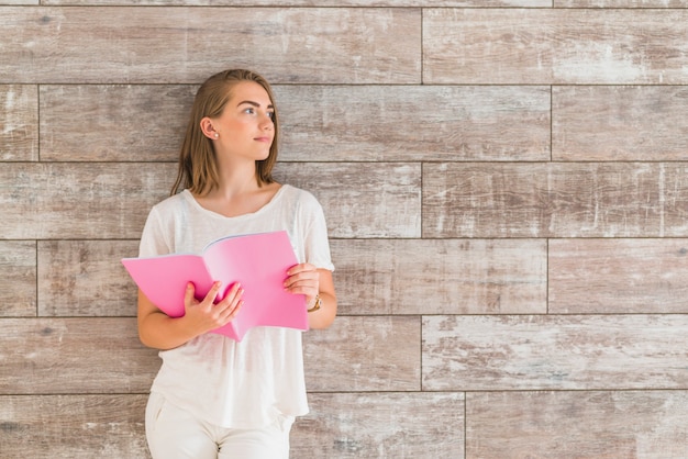 Retrato de mujer de pie delante de la pared sosteniendo el libro rosa mirando a otro lado