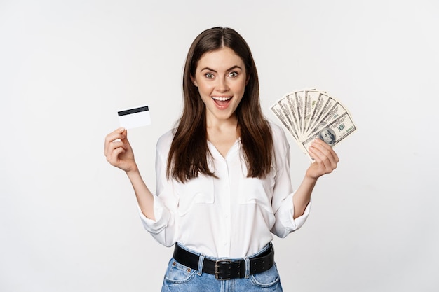 Retrato de mujer de pie con efectivo y tarjeta de crédito, concepto de dinero, microcrédito y préstamos, de pie sobre fondo blanco feliz