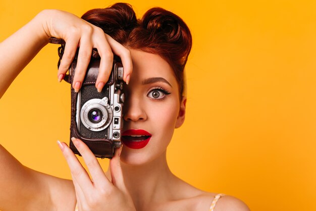 Retrato de mujer pinup asombrada con cámara. Fotógrafo encantador con labios rojos tomando fotografías.