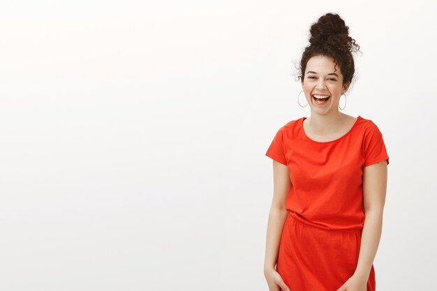 Retrato de mujer positiva de aspecto agradable con cabello rizado en elegante vestido rojo, riendo a carcajadas y riendo de felicidad