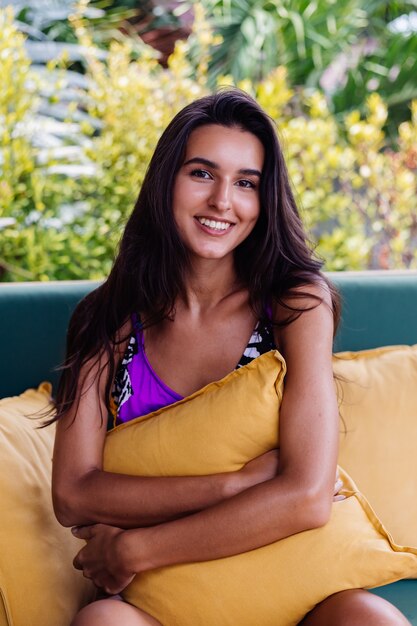 Retrato de mujer positiva delgada bastante en forma descansando con almohada en casa en el sofá de verano al aire libre, disfrutando del tiempo solo