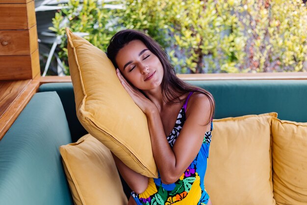 Retrato de mujer positiva delgada bastante en forma descansando con almohada en casa en el sofá de verano al aire libre, disfrutando del tiempo solo