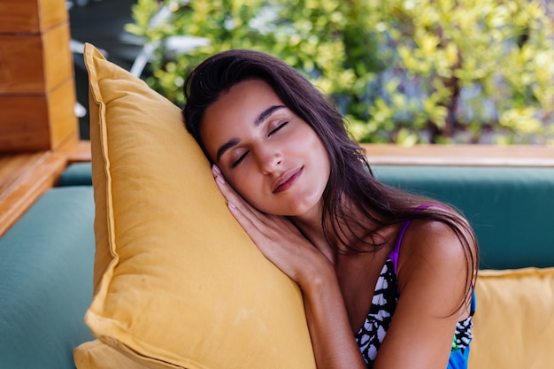 Foto gratuita retrato de mujer positiva delgada bastante en forma descansando con almohada en casa en el sofá de verano al aire libre, disfrutando del tiempo solo