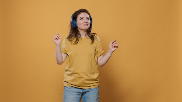 Retrato de mujer positiva llena de energía con auriculares inalámbricos haciendo fiesta y bailando sola en el estudio. Mujer casual escuchando música alegre en los auriculares y haciendo movimientos de baile extravagantes.