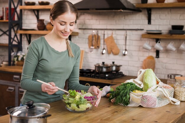 Retrato de mujer positiva preparando una ensalada fresca