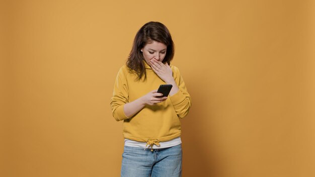 Retrato de una mujer preocupada que sostiene mensajes de texto con un teléfono inteligente y tiene una conversación seria en línea en la aplicación de mensajería de las redes sociales en el estudio. Persona ansiosa de unos 20 años que usa un dispositivo de pantalla táctil digital.