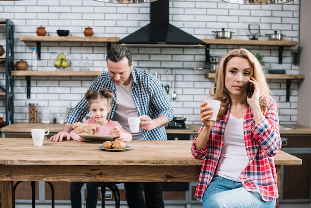 Retrato de una mujer que habla en el teléfono móvil que sostiene la taza de café en cocina