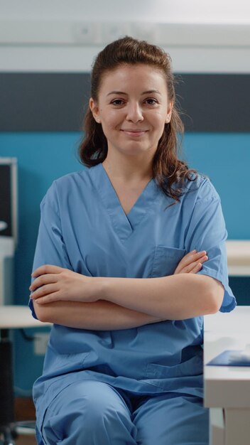 Retrato de mujer que trabaja como asistente médico en el escritorio de la oficina de médicos. Enfermera mirando a la cámara y sonriendo mientras se prepara para trabajar en la computadora. Especialista en salud en uniforme