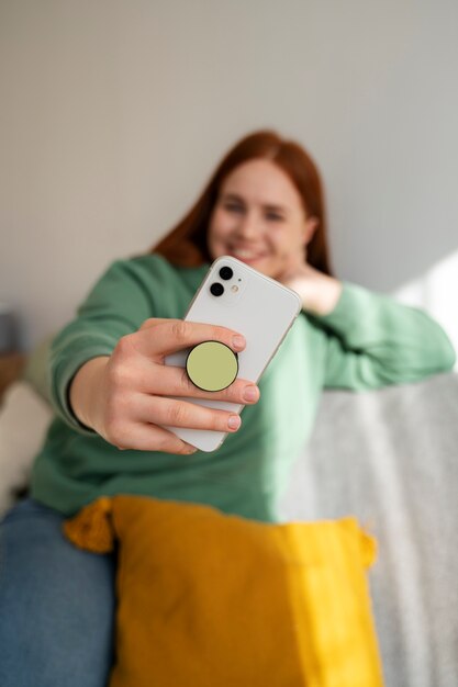 Retrato de una mujer que usa su teléfono inteligente en casa en el sofá sosteniéndolo de una toma de corriente