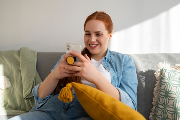 Foto gratuita retrato de una mujer que usa su teléfono inteligente en casa en el sofá sosteniéndolo de una toma de corriente