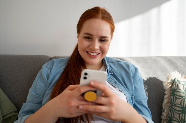 Retrato de una mujer que usa su teléfono inteligente en casa en el sofá sosteniéndolo de una toma de corriente