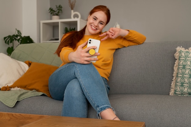 Foto gratuita retrato de una mujer que usa su teléfono inteligente en casa en el sofá sosteniéndolo de una toma de corriente