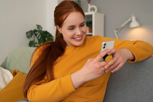 Retrato de una mujer que usa su teléfono inteligente en casa en el sofá sosteniéndolo de una toma de corriente