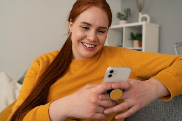 Retrato de una mujer que usa su teléfono inteligente en casa en el sofá sosteniéndolo de una toma de corriente