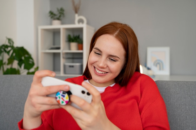 Retrato de una mujer que usa su teléfono inteligente en casa en el sofá sosteniéndolo de una toma de corriente