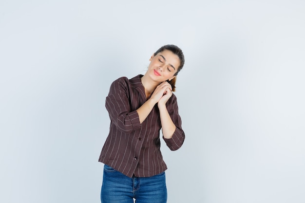 Retrato de mujer recostada sobre las manos como almohada en camisa, jeans y mirando soñoliento vista frontal