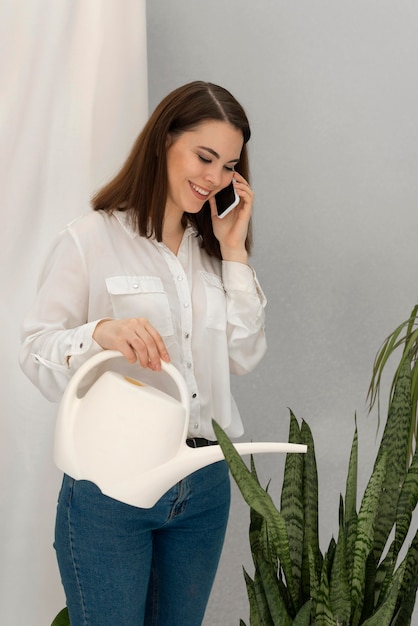 Retrato mujer regando la planta mientras habla por móvil