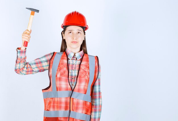 Retrato de mujer reparadora en uniforme con martillo sobre pared blanca.