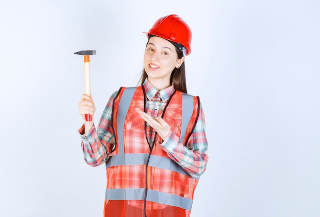 Retrato de mujer reparadora en uniforme de pie con un martillo sobre la pared blanca.