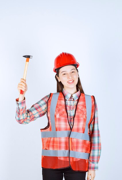 Retrato de mujer reparadora en uniforme de pie con un martillo sobre la pared blanca.