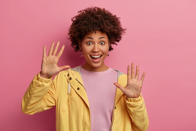 Retrato de mujer rizada alegre mantiene las palmas levantadas, disfruta del tiempo libre