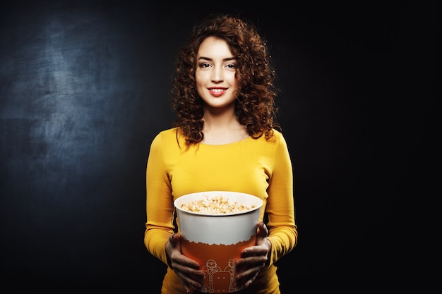 Retrato de mujer rizada con cubo de palomitas de maíz mirando directamente