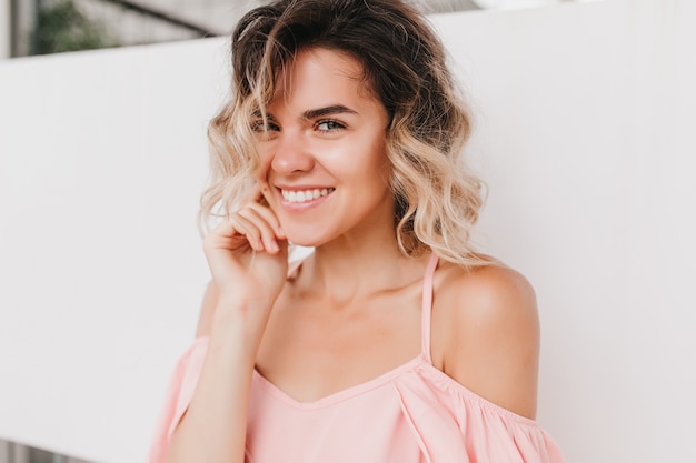 Retrato de mujer rubia encantadora en ropa rosa posando juguetonamente. Foto de primer plano de dama refinada con peinado ondulado.