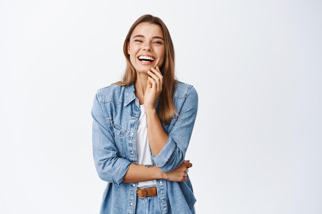 Retrato de mujer rubia feliz en ropa casual, riendo y divirtiéndose, sonriendo alegre, de pie en blanco