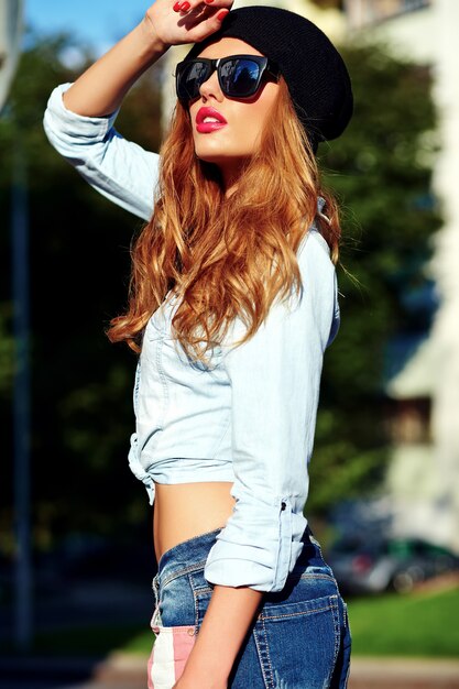 Retrato de mujer rubia hermosa modelo hipster en ropa casual de verano con estilo azul jeans en gafas de sol posando en la calle