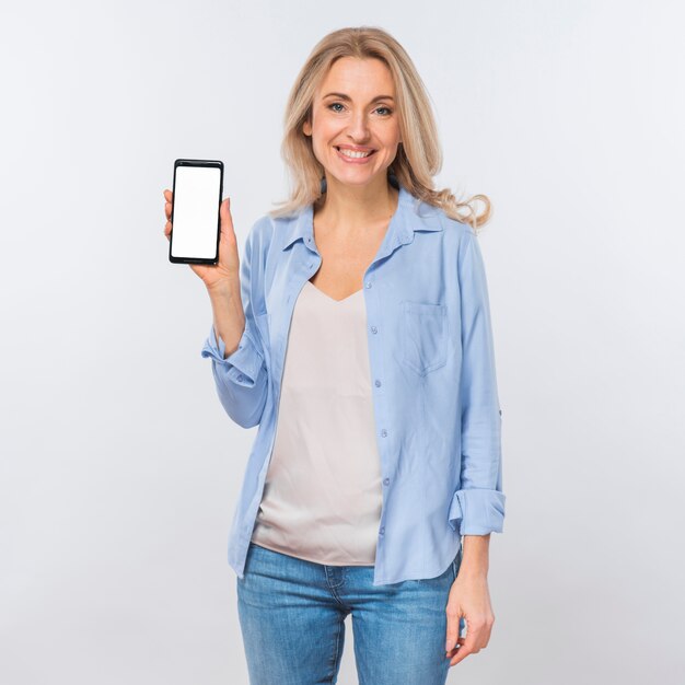 Retrato de una mujer rubia joven que mira la cámara que muestra el teléfono móvil con la pantalla blanca en blanco