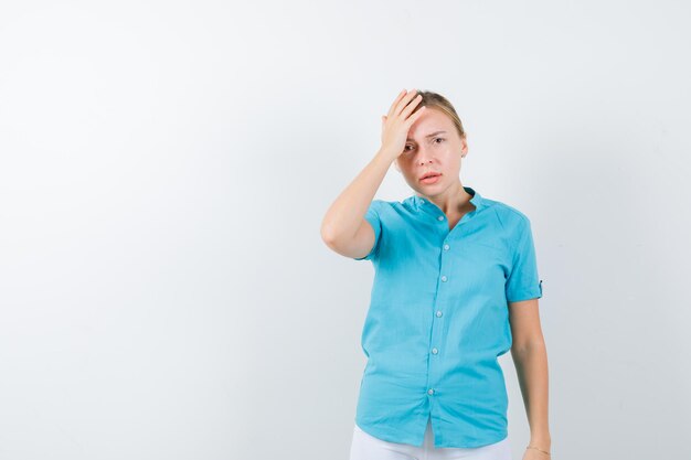 Retrato de mujer rubia manteniendo la mano en la cabeza en blusa azul aislado