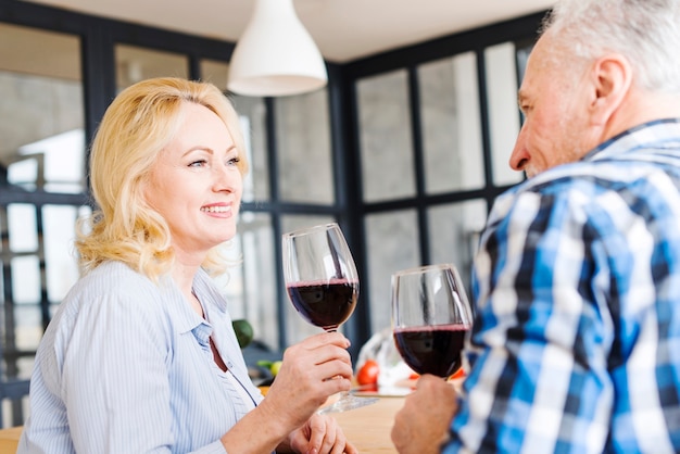 Retrato de una mujer rubia mayor que bebe el vino con su marido en la cocina