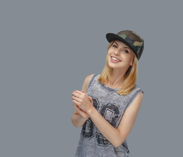 Retrato de mujer rubia positiva con gorra de béisbol. Aislado sobre fondo gris.