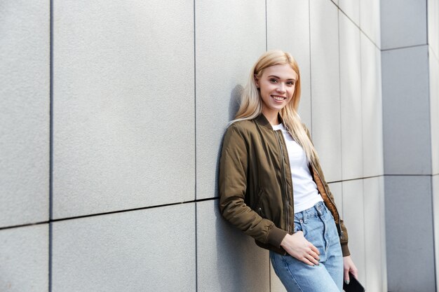 Retrato de mujer rubia sonriente contra la pared gris