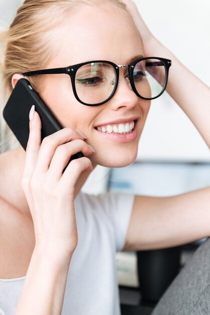 Retrato de mujer rubia sonriente hablando por teléfono inteligente