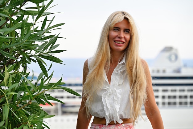 Foto gratuita retrato de una mujer rubia sonriente en mónaco cerca de un árbol mirando a la cámara puerto marítimo