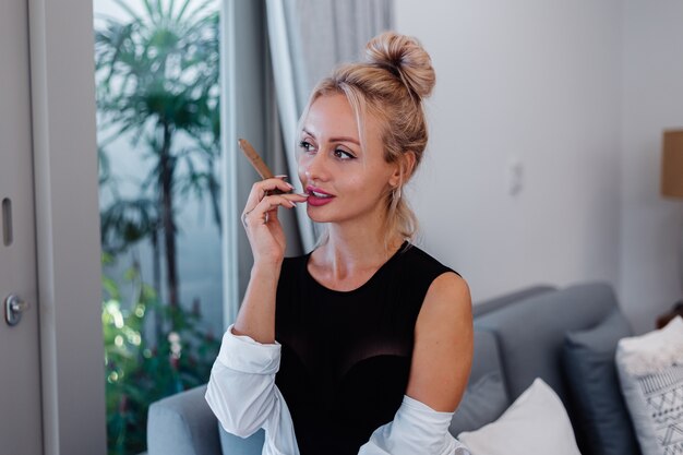 Retrato de mujer rubia en traje de cuerpo y camisa blanca con hermosos labios rosados con cigarro