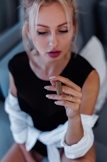 Retrato de mujer rubia en traje de cuerpo y camisa blanca con hermosos labios rosados con cigarro