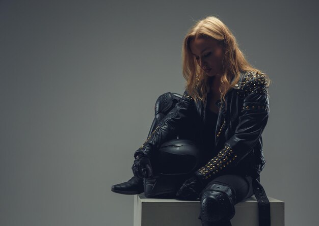 Retrato de mujer rubia con traje de motocicleta de cuero sobre fondo gris en un estudio.