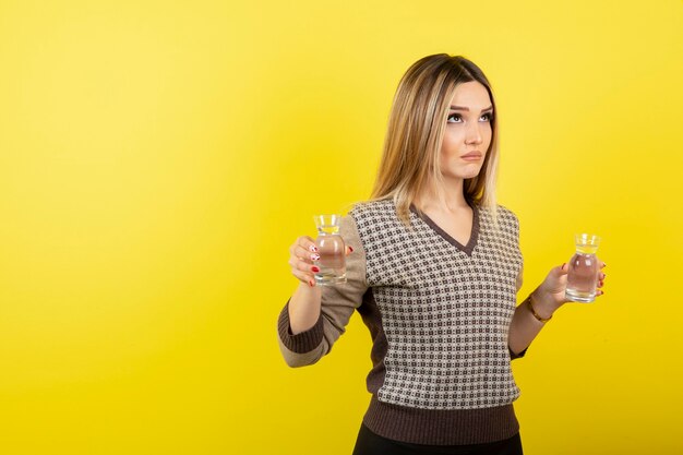 Retrato de mujer rubia con vaso de agua en amarillo.