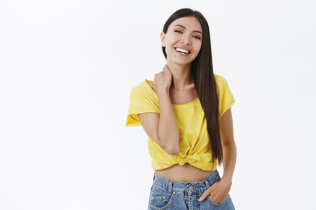 Retrato de mujer saliente de aspecto amable alegre con cabello oscuro en elegante camiseta amarilla sosteniendo la mano en el bolsillo