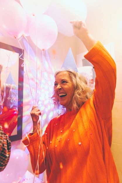 Retrato de una mujer senior feliz sosteniendo globos en la mano disfrutando en la fiesta de cumpleaños