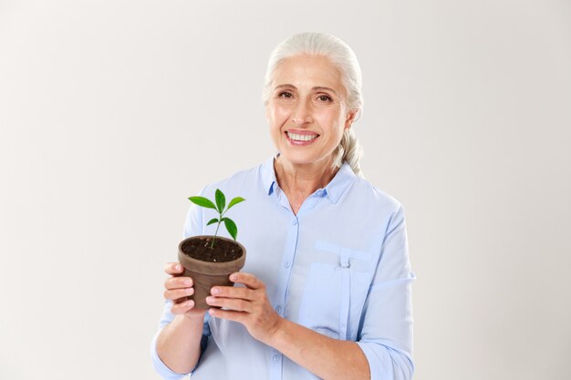 Retrato de mujer senior feliz, sosteniendo maceta con planta verde