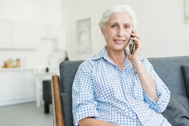 Retrato de mujer senior hablando por teléfono móvil en casa