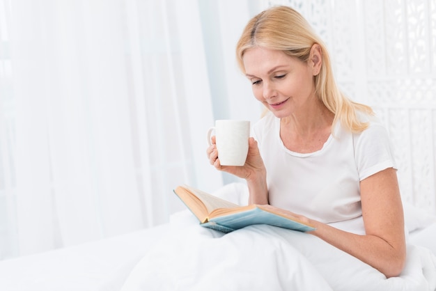 Retrato de mujer senior leyendo un libro en la cama