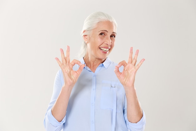 Retrato de mujer senior sonriente en camisa azul mostrando gesto OK